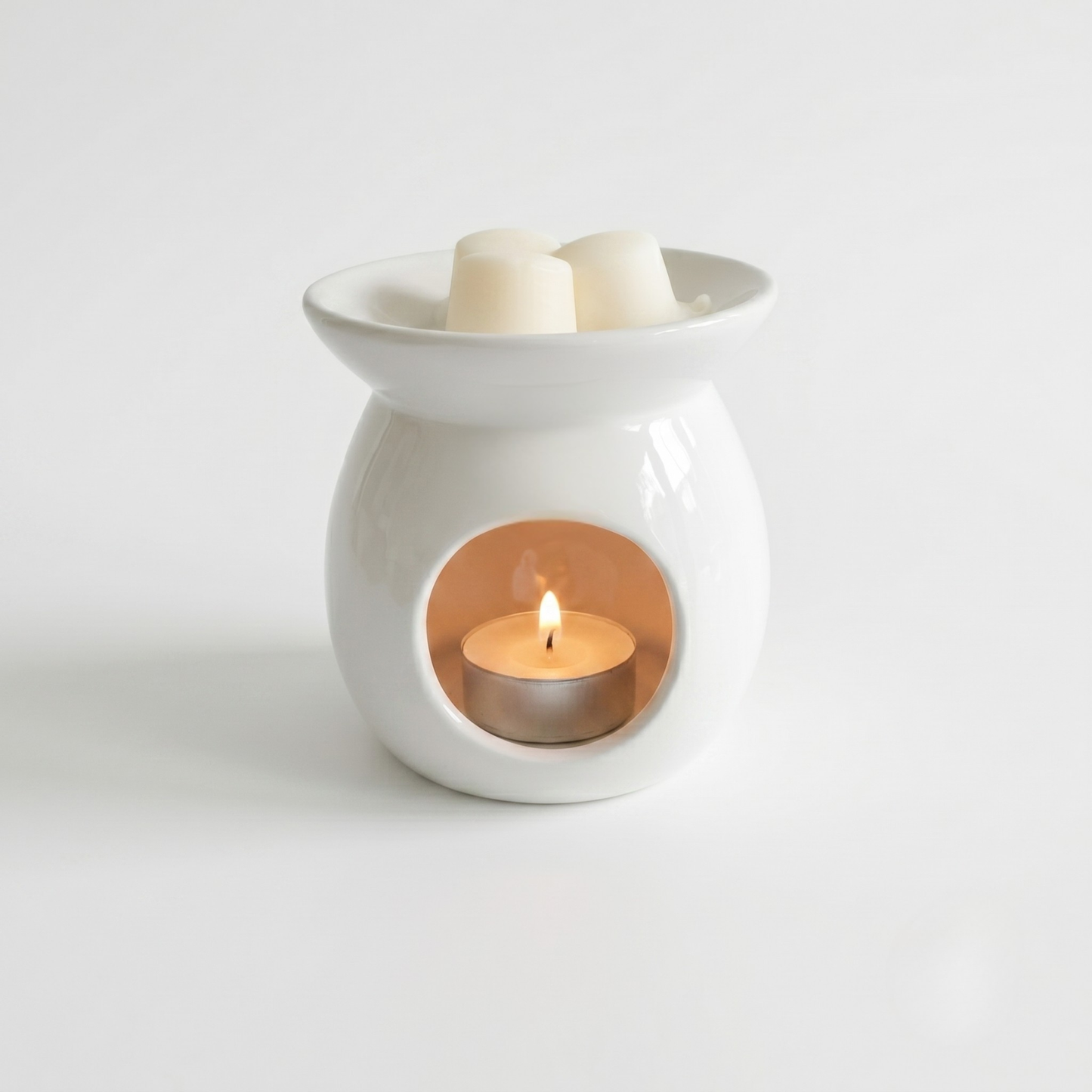 White ceramic wax warmer with a lit candle inside on a light gray background