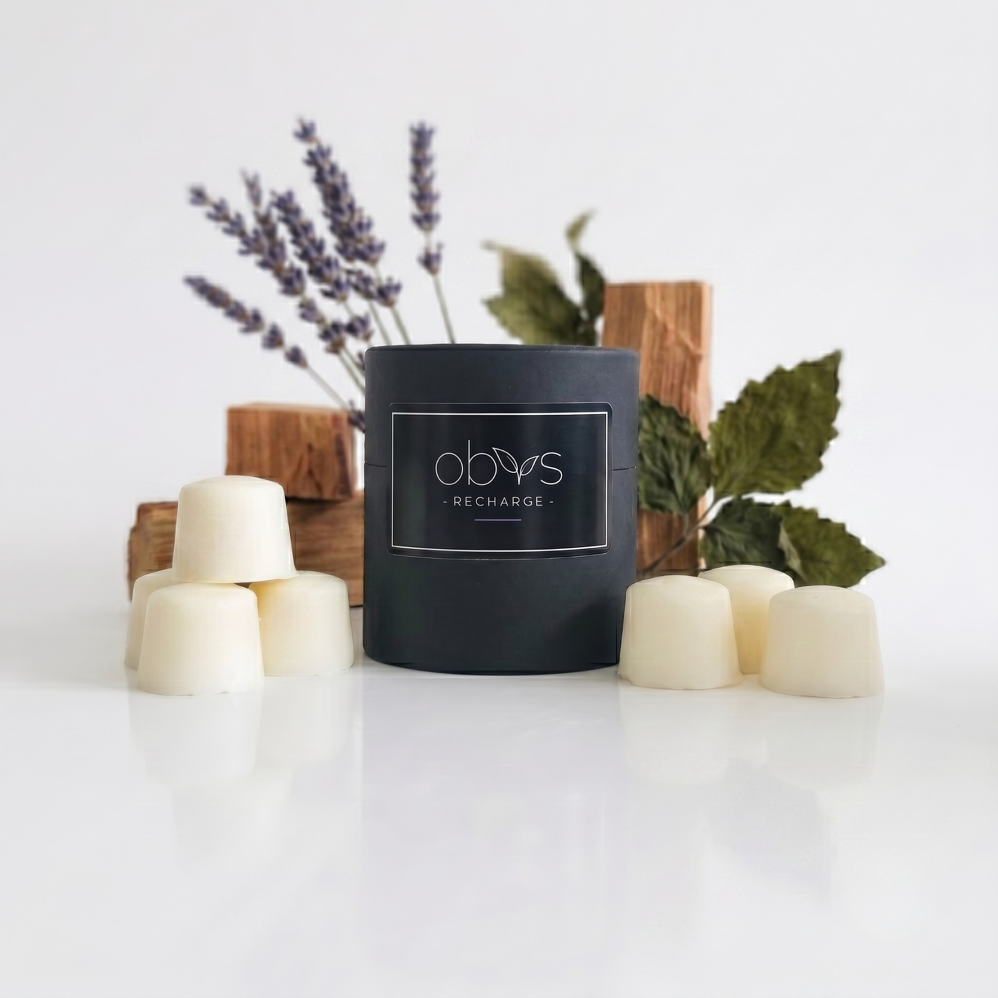 Black wax melts labeled 'obvs recharge' with wooden blocks and lavender on a white background