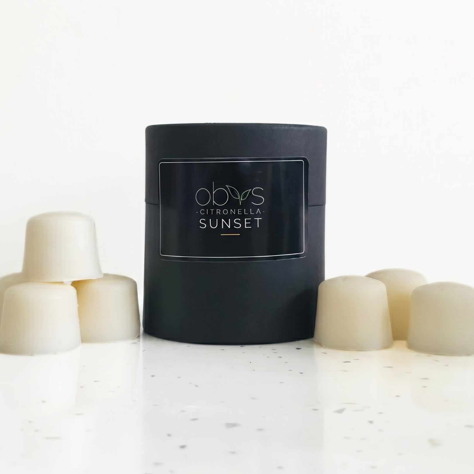 Black wax melt container labeled 'Citronella Sunset' on a white surface with white candles.