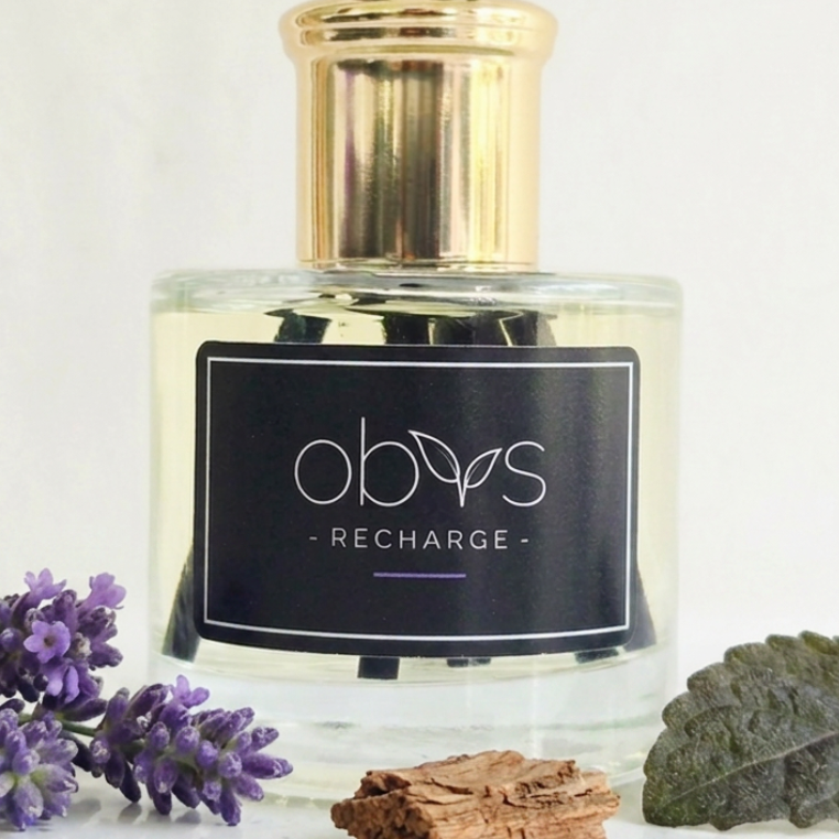 A bottle of OBVS recharge diffuser with lavender flowers and leaves on a light background