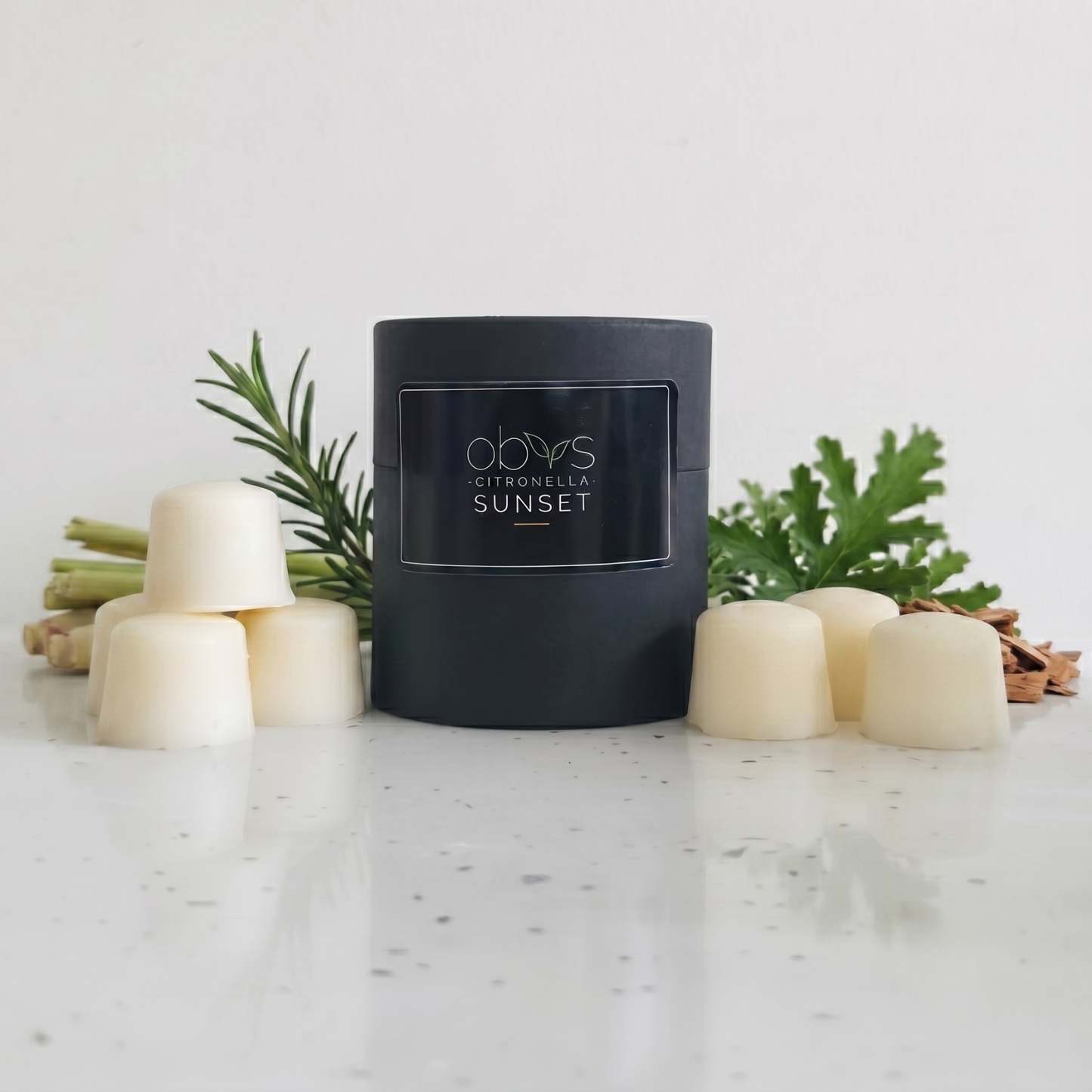 Black wax melt container labeled 'Citronella Sunset' on a marble surface with decorative elements.
