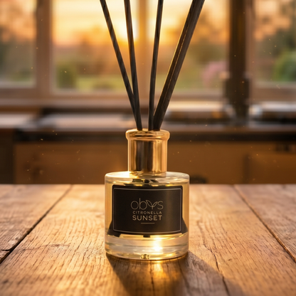 Reed diffuser labeled 'Citronella Sunset' on a wooden surface with a blurred background