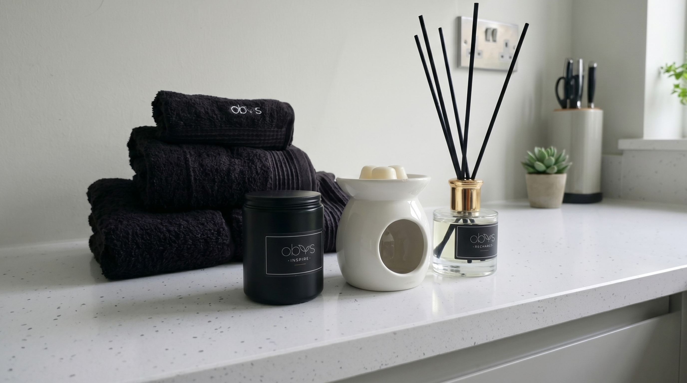 Black towels, candles, and diffuser on a white surface with a neutral background