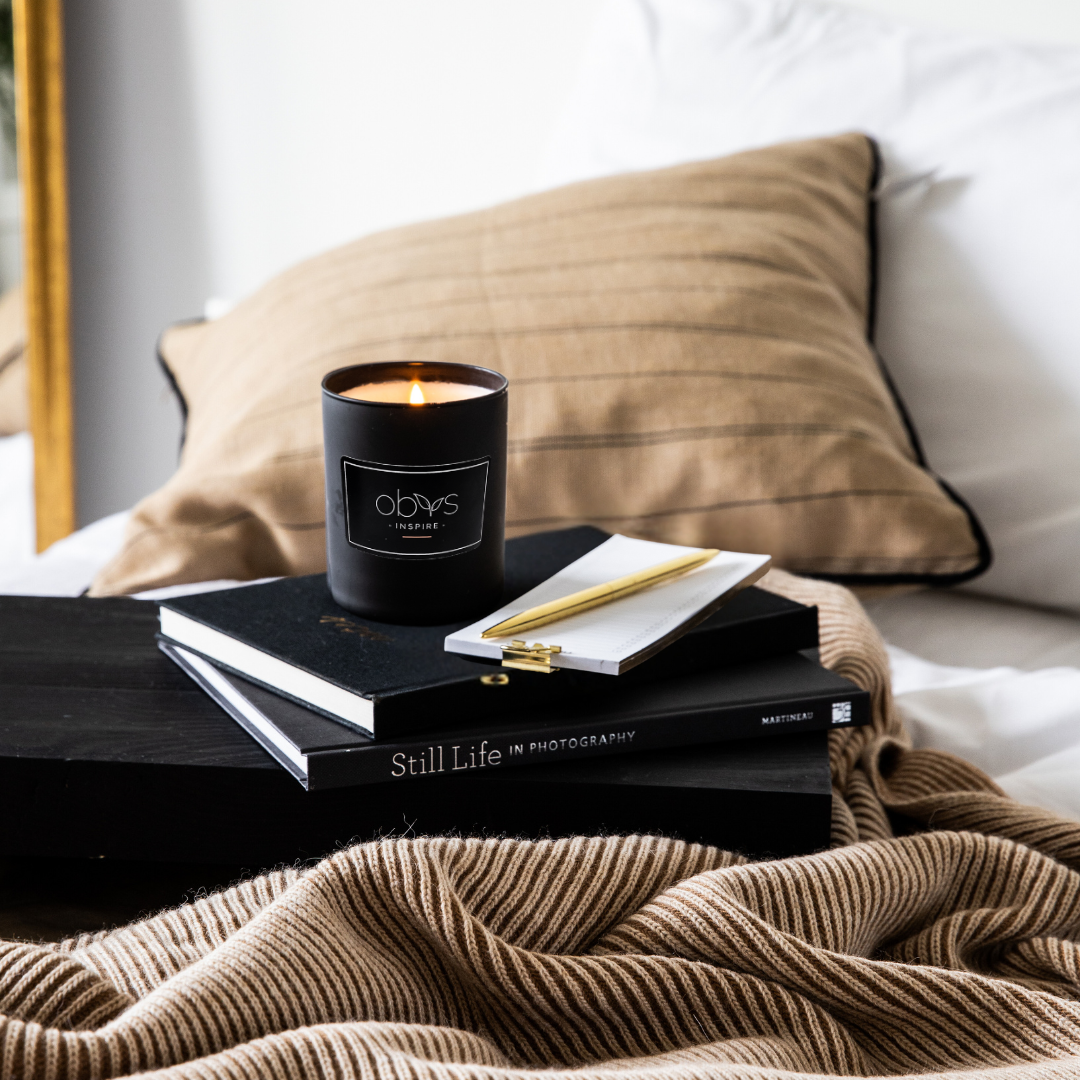 A matte black candle jar filled with organic essential oils, burning with a soft, warm flame. The minimalist design exudes elegance, while the gentle aroma from natural essential oils creates a calming, eco-friendly atmosphere. The candle sits on a wooden surface, with subtle shadows enhancing its luxurious, earthy vibe, perfect for relaxation or meditation