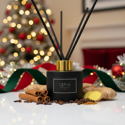 Black diffuser with gold cap on a table in front of a decorated Christmas tree. Obvs Skincare Christmas Reed Diffuser with cinnamon, clove and ginger essential oils on a festive background